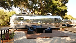 A silver recreational vehicle with a patio area featuring outdoor furniture and planters. - Village Inn  (Lompoc)