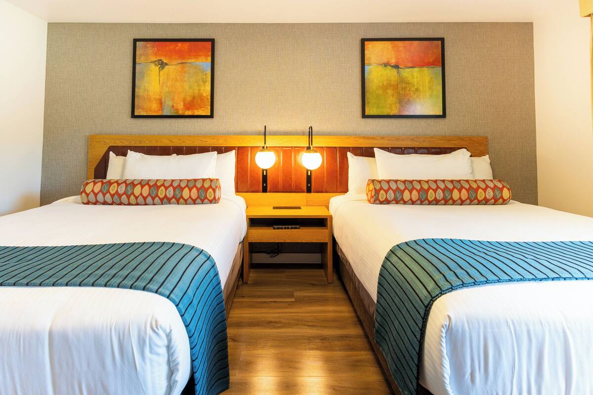 A hotel room with two beds, a wooden headboard, and two wall-mounted paintings.