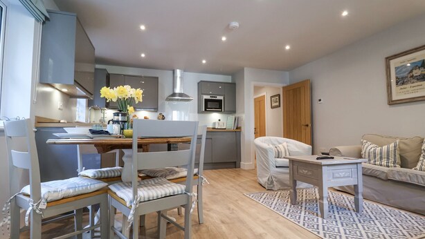 A modern kitchen with grey cabinets, a central island, and a dining area with a wooden table and chairs. - Bradley's Barn (Colchester)