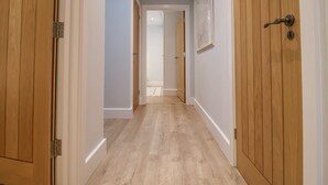 A hallway with wooden doors, white walls, and a light wooden floor. - Bradley's Barn (Colchester)