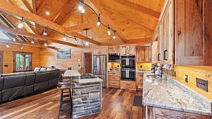 A spacious log cabin interior with a stone island, wooden cabinets, and a large sofa.