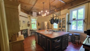 Une cuisine dotée d’un grand îlot central, d’un plafond en bois et de casseroles suspendues.