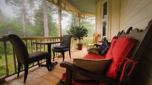 Une véranda avec un plancher en bois, une table, deux chaises, un banc rouge avec coussin et une plante en pot.