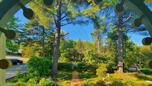 Un chemin qui traverse un jardin agrémenté d’arbres et d’arbustes, avec une clôture blanche et une voiture garée sur le côté.