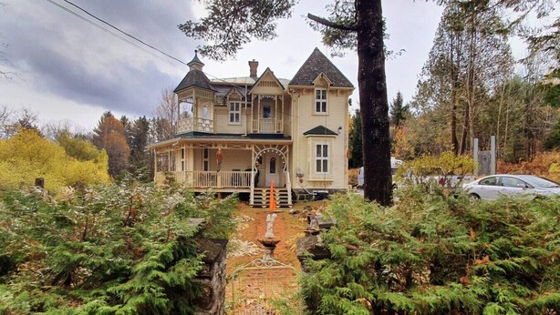Une maison à deux étages avec une véranda qui fait le tour de la maison, entourée d’épais arbres à feuilles persistantes.