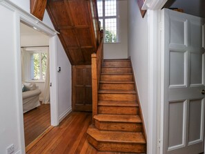 Eine Holztreppe führt zu einer Zwischenebene mit einer Tür rechts und einem Fenster darüber.