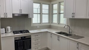 Une cuisine moderne avec des meubles blancs, une cuisinière à gaz, un évier et une fenêtre donnant sur l’extérieur.
