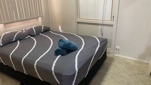 Ein ordentlich bezogenes Bett mit dunkelgrauer und weißer Streifenoptik, zwei Kissen und zwei zusammengerollte Handtücher.