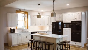 Une cuisine moderne avec des meubles blancs, un grand îlot central doté de tabourets, des appareils en acier inoxydable et un éclairage suspendu.