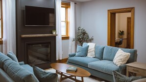 Un salon avec une cheminée, un canapé bleu, une table basse et un téléviseur fixé au mur.