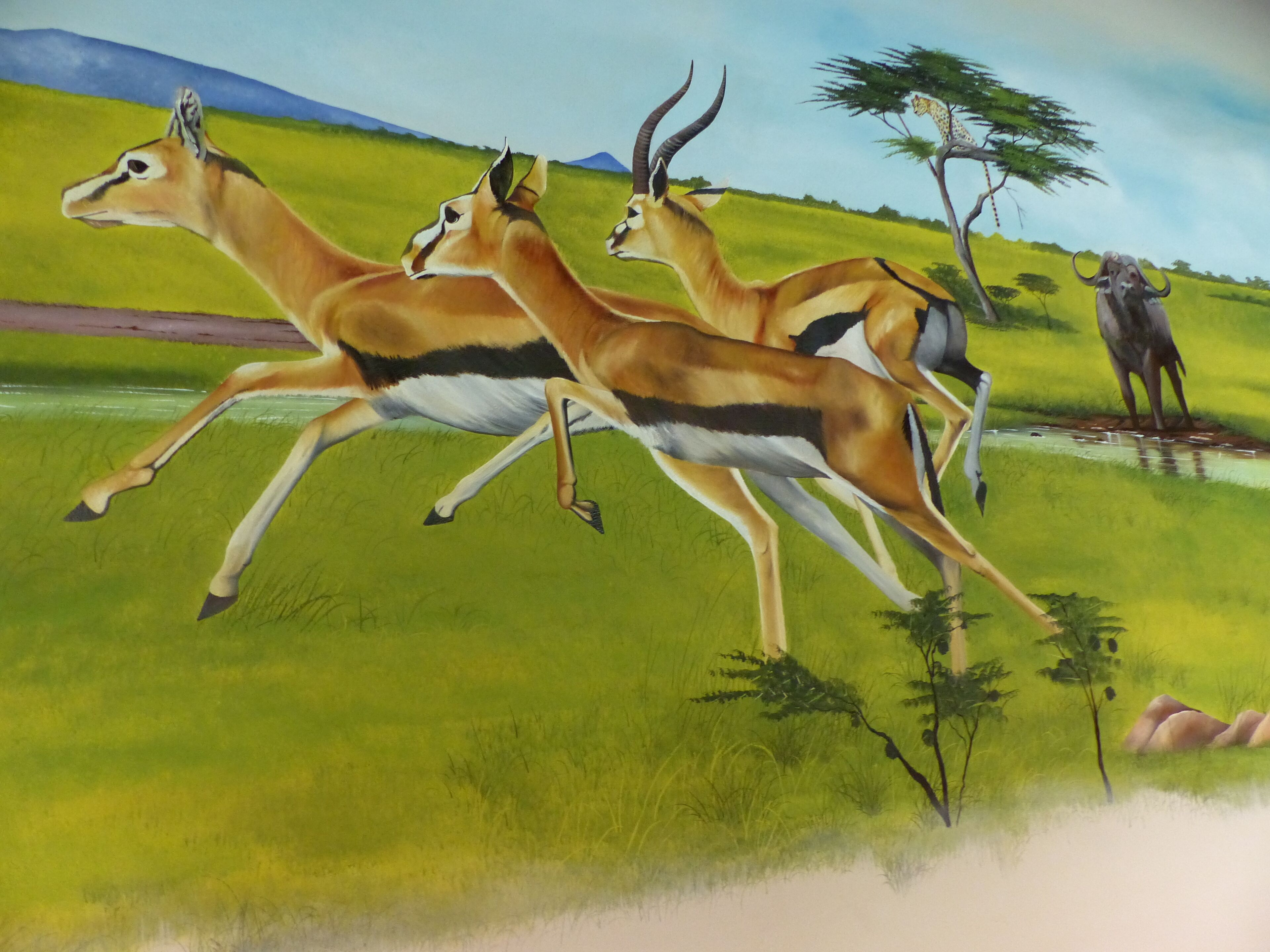 Un mural d'antílops corrent en un prat amb arbres i una girafa al fons.