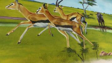 Un mural d'antílops corrent en un prat amb arbres i una girafa al fons.