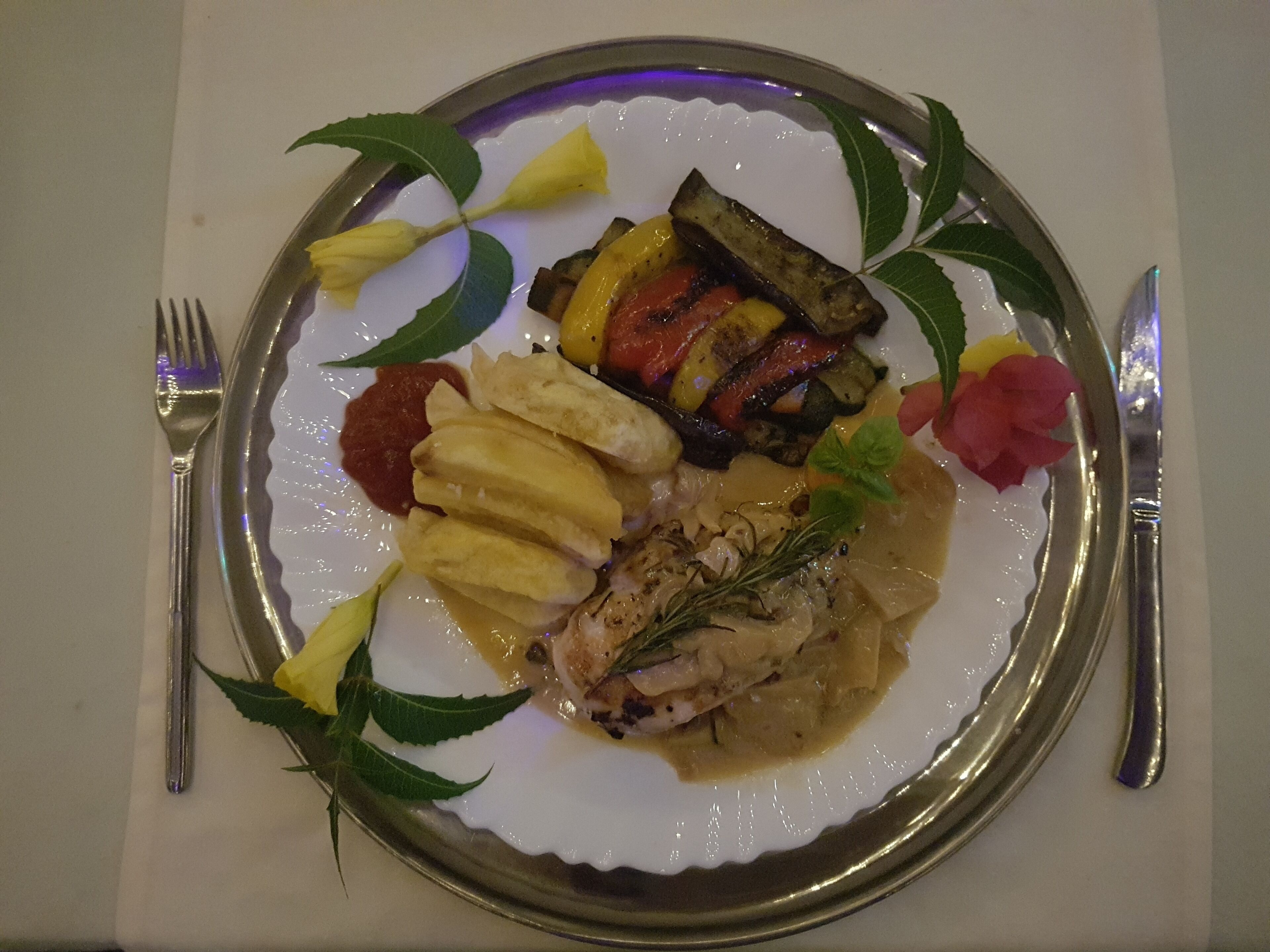 A plate of food with various vegetables and a piece of meat, accompanied by a fork and knife on a table.