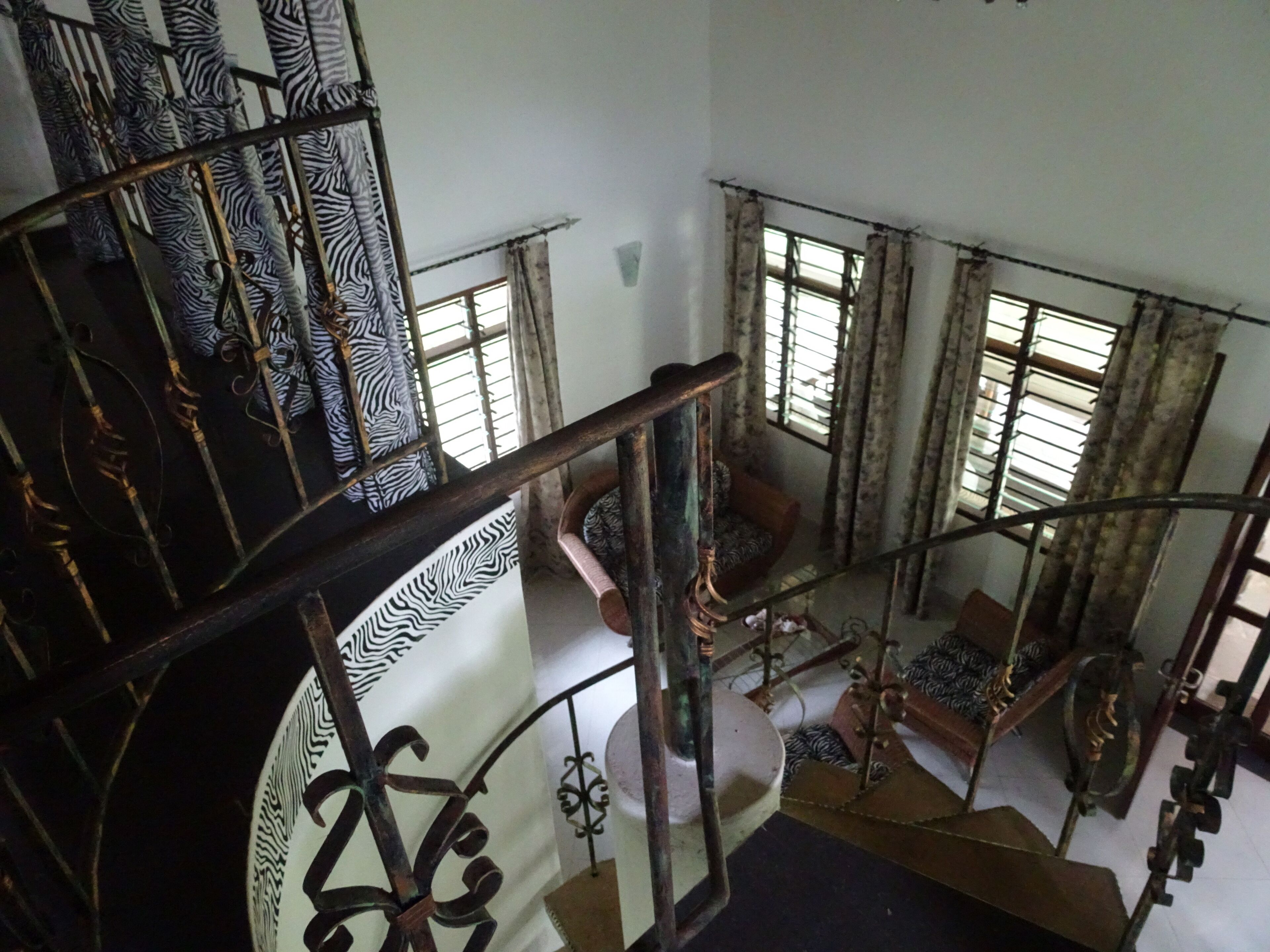 A multi-level interior with a spiral staircase, zebra-patterned curtains, and a round chair in the lower level.