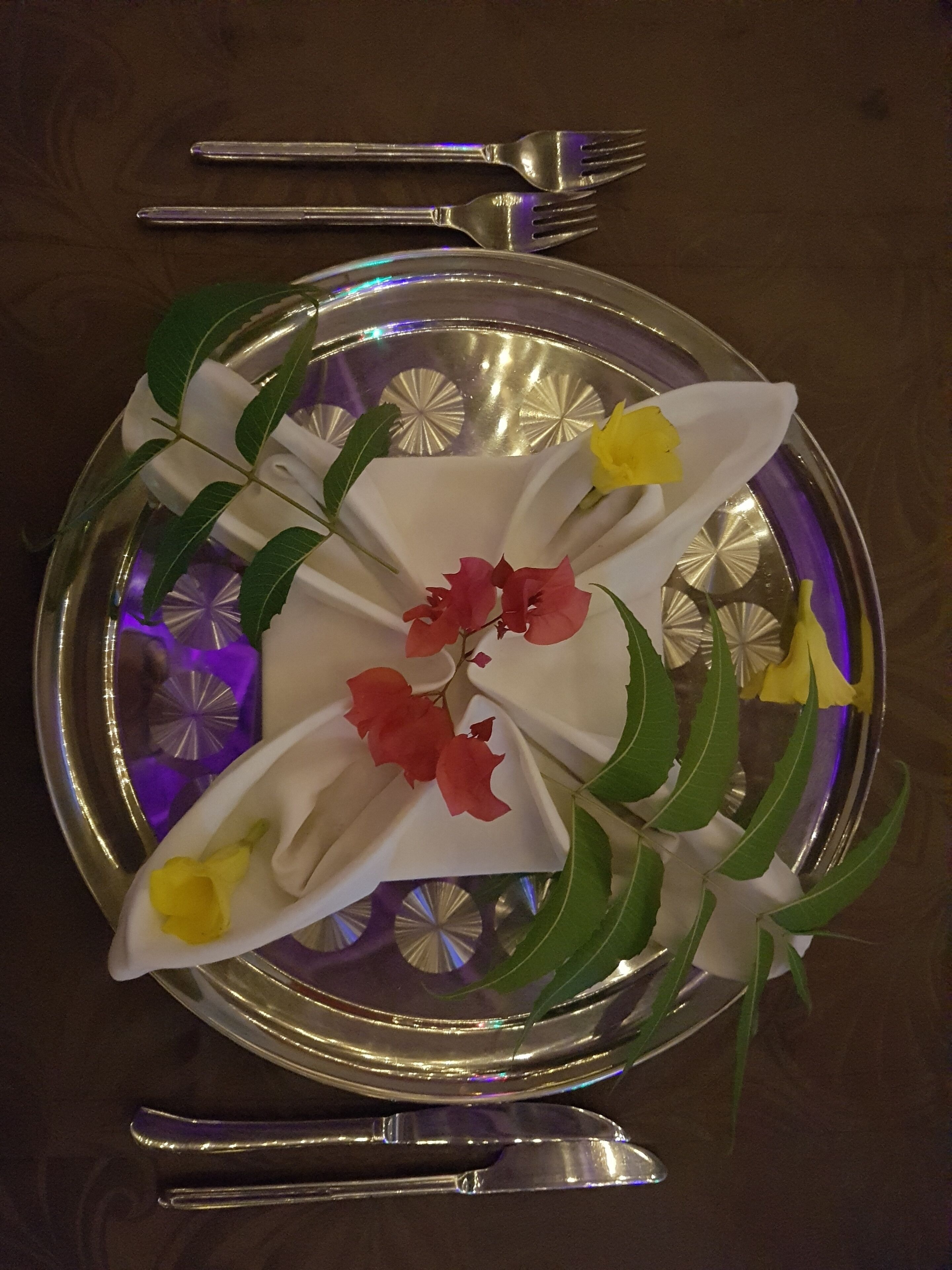 Une table dressée avec une assiette décorative, des couverts en argent et une serviette pliée.