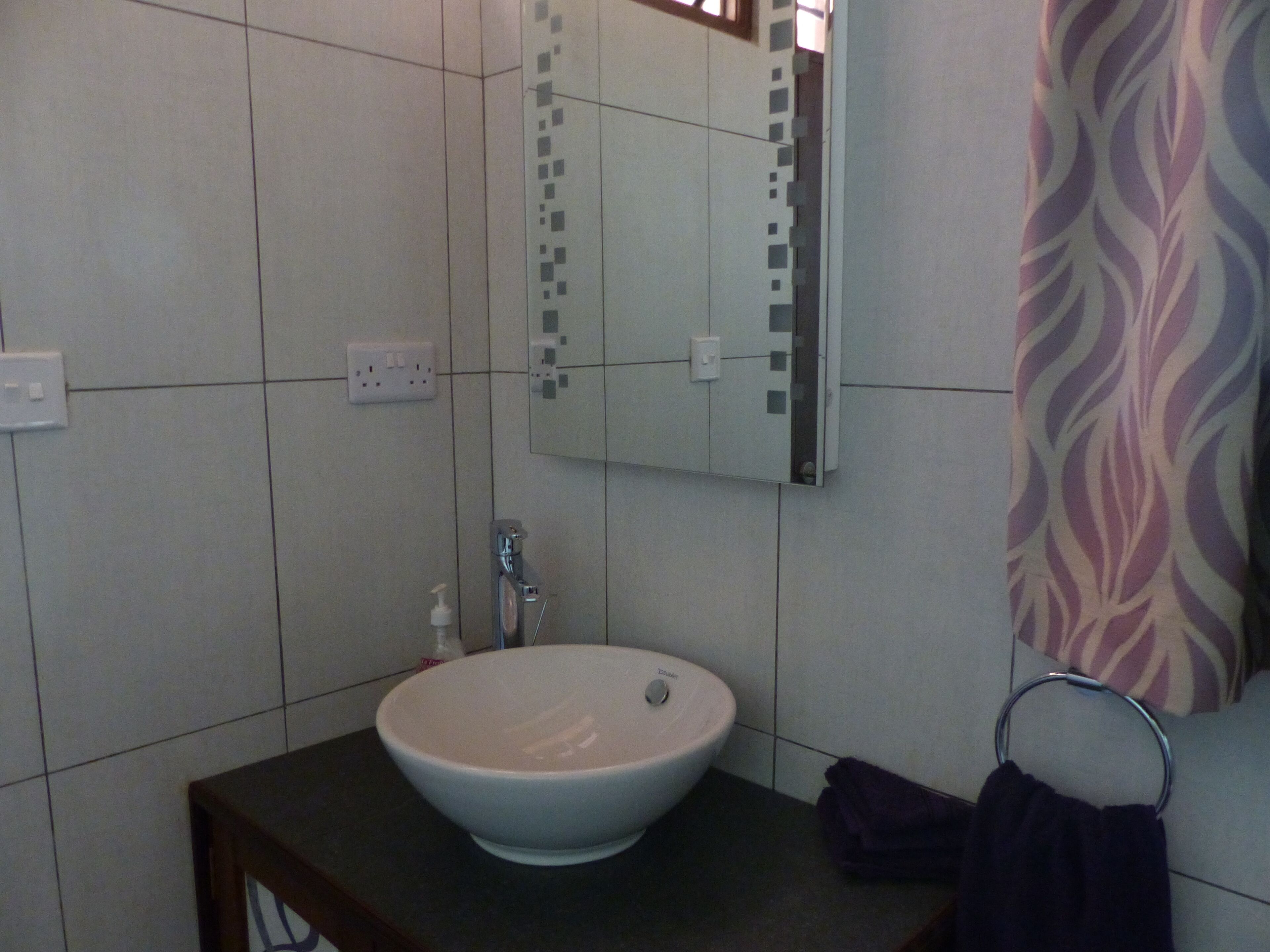 Un baño con un lavabo blanco, un espejo y un perchero para toallas.