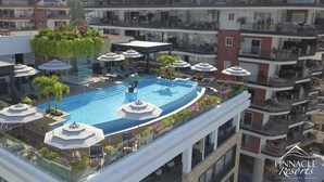 A rooftop pool with sun loungers and umbrellas, surrounded by balconies and greenery.