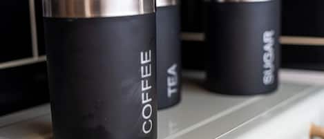 Three black containers labeled "COFFEE," "TEA," and "SUGAR" on a shelf.