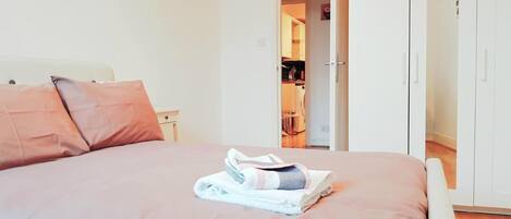A neatly made bed with a folded towel and a pillow, a wardrobe, and a door leading to a kitchen area.