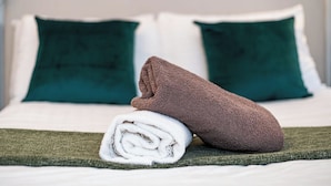 Un lit bien fait, avec une serviette marron et une serviette blanche roulée posées sur un couvre-lit vert.