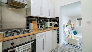 Une cuisine de taille réduite avec des meubles blancs, une cuisinière à gaz, un four à micro-ondes et un évier.
