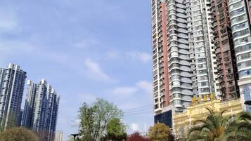 A high-rise building with multiple balconies, surrounded by trees and other buildings.