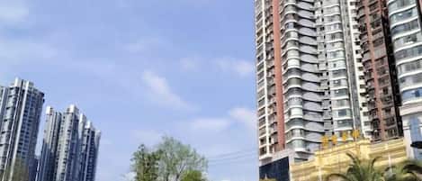 Un edificio alto con varios balcones, rodeado de árboles y otros edificios.