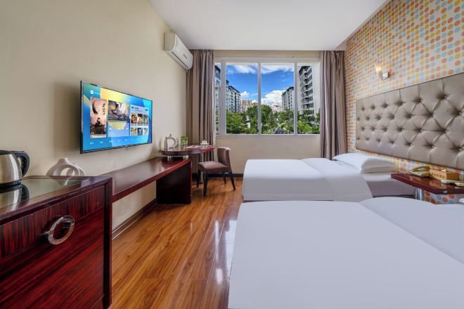 A hotel room with a bed, desk, chair, TV, and a window with a city view.