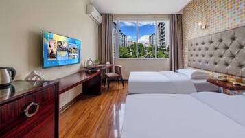 A hotel room with a bed, desk, chair, TV, and a window with a city view.