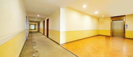 A hotel corridor with carpeted flooring, doors, and an elevator.