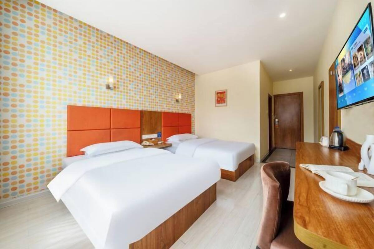 A hotel room with two beds, a wooden headboard, a desk with a coffee maker, and a TV on the wall.