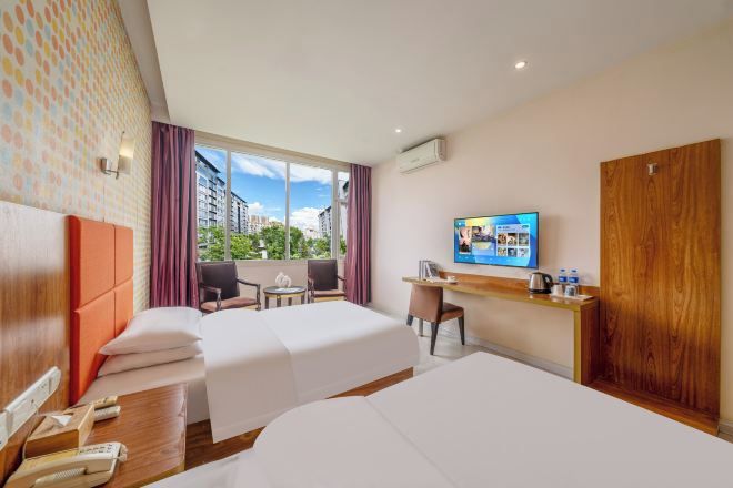 A hotel room with two beds, a desk, a chair, a TV, and a window with a city view.