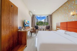 A hotel room with a bed, a desk, a TV, and a view of buildings through the window. - Tongren Rujia Hotel (Tongren)