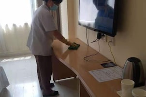 A person cleaning a wooden counter with a cloth, a television mounted on the wall, and a kettle on the counter.