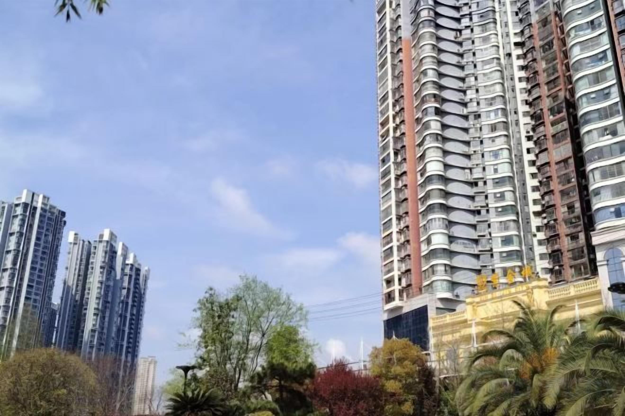 Edificios residenciales altos con balcones, rodeados de árboles y vegetación.
