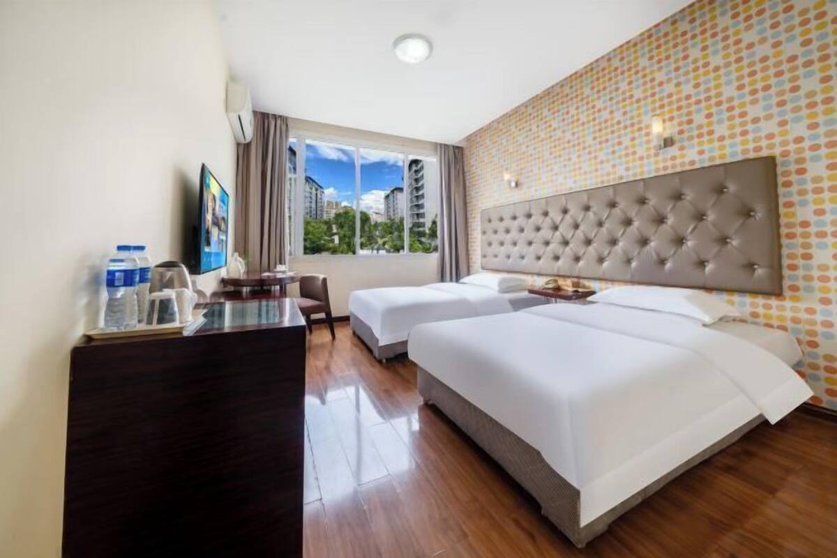 A hotel room with two beds, a desk, a chair, a television, and a large window with a view of buildings.