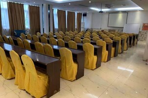Un salón de conferencias con filas de mesas y sillas, una pantalla de proyector y una pizarra.