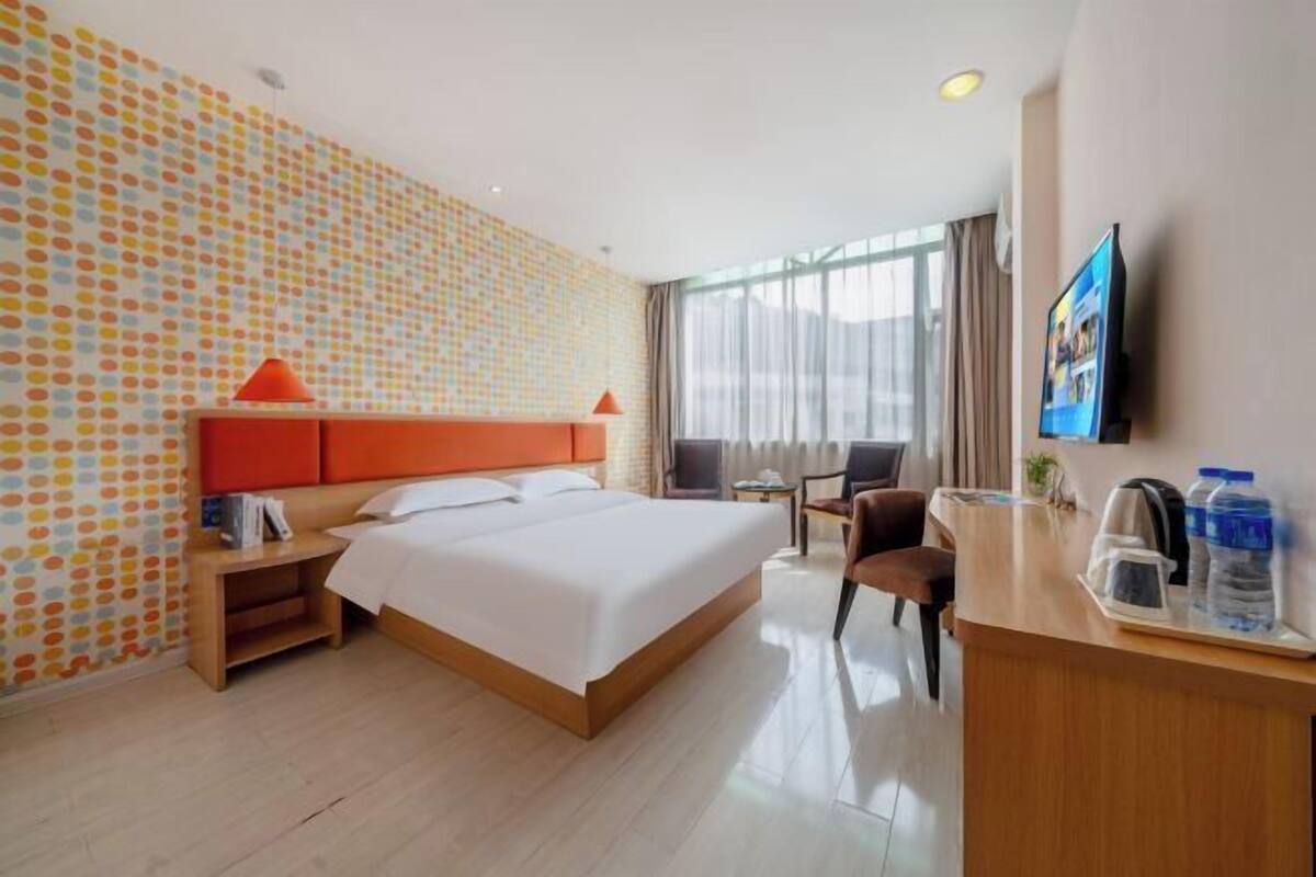 A hotel room with a large bed, a desk with a chair, a TV, and a window with curtains.
