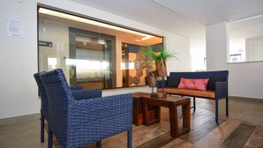 A lobby with wicker chairs, a wooden table, and a sofa with a red cushion.