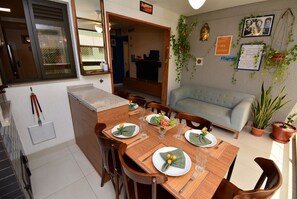 A dining area with a wooden table set for four, chairs, and a sofa in the background. - Spazio di Palmas a 300 metros da praia (Governador Celso Ramos)