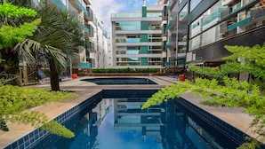 A modern apartment building with a central swimming pool, surrounded by greenery and outdoor seating areas.