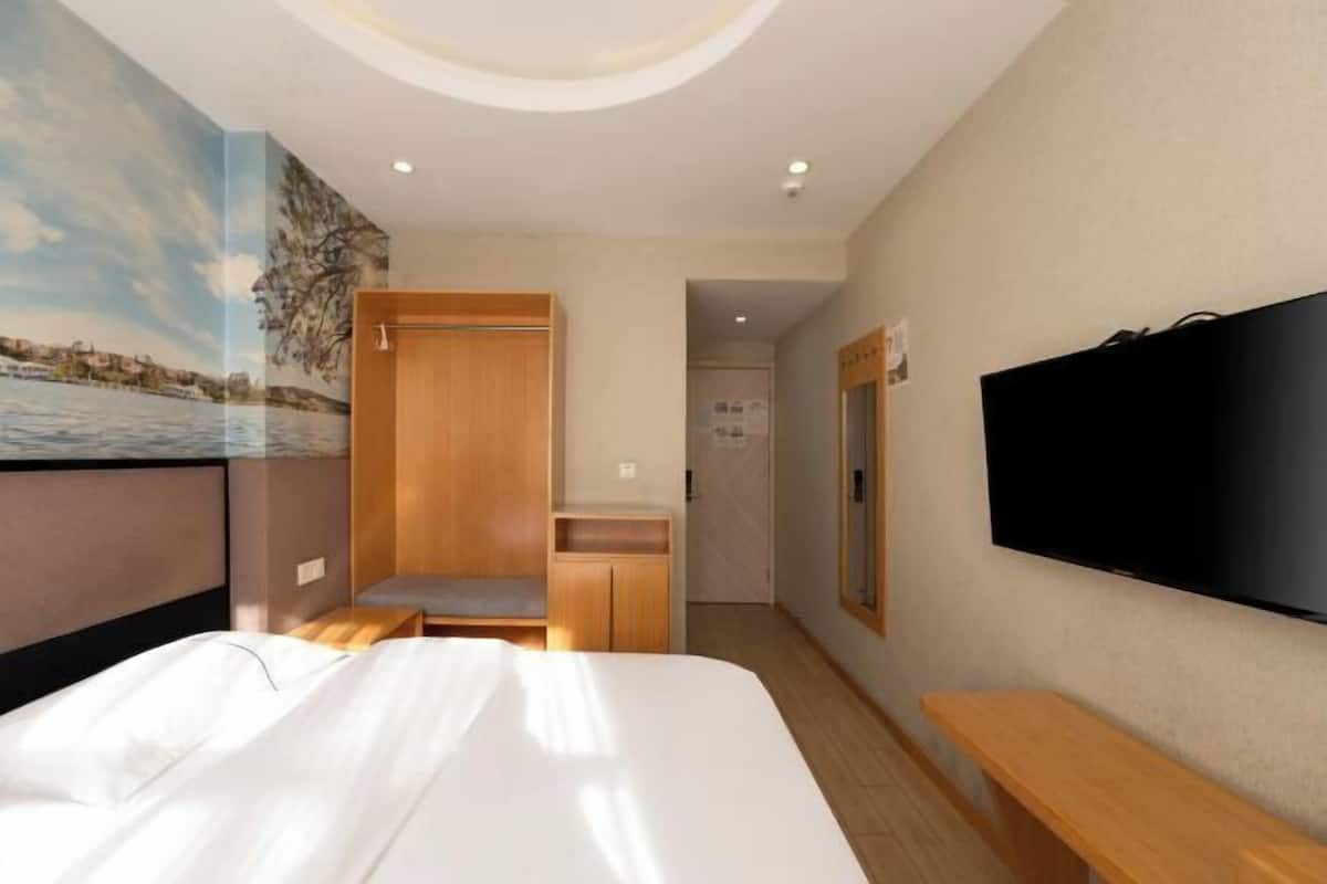 Ein Hotelzimmer mit einem Bett, einem Fernseher, einer hölzernen Bank, einem Kleiderschrank und einem Wandgemälde.