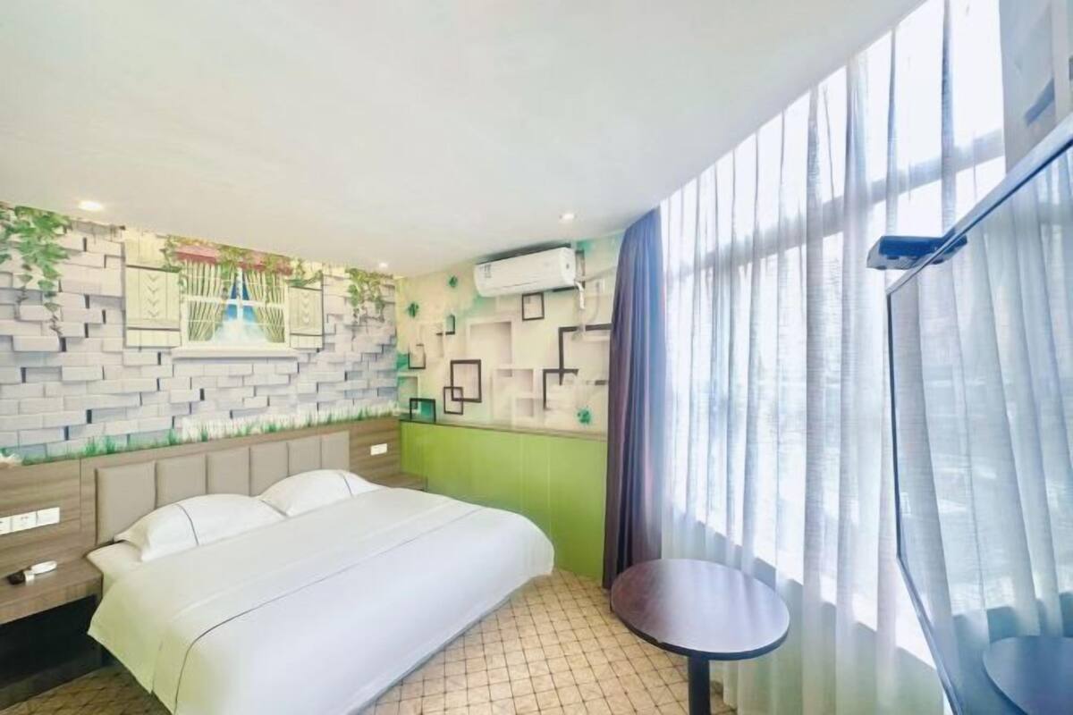 Ein Hotelzimmer mit einem Bett, einem kleinen Tisch, einer wandmontierten Klimaanlage und einem fensterbepflanzten Fenster.