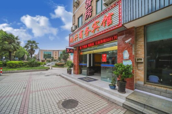 A hotel with a red sign, a paved entrance, and a small garden area. - Hongxing Business Hotel (Shanghai)