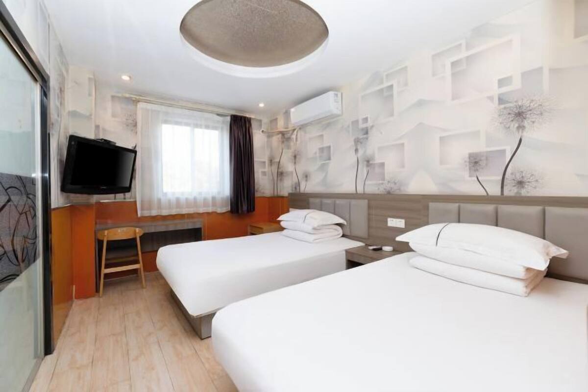 Ein Hotelzimmer mit zwei Betten, einem Fernseher, einem kleinen Tisch und einem Fenster mit Vorhängen.