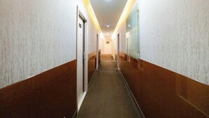 Un pasillo largo y estrecho con puertas a ambos lados, que conduce a habitaciones. El pasillo tiene piso alfombrado y está iluminado por luces del techo.