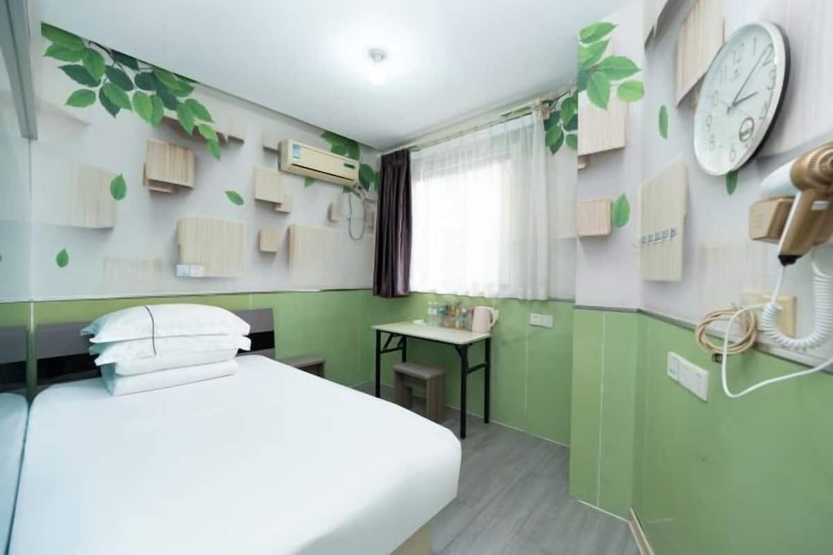Ein Hotelzimmer mit einem Bett, einem kleinen Tisch, einem Sessel, einer Uhr und einem Telefon an der Wand.