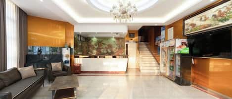 Um saguão de hotel com balcão de recepção, área de estar e escadaria para os andares superiores.
