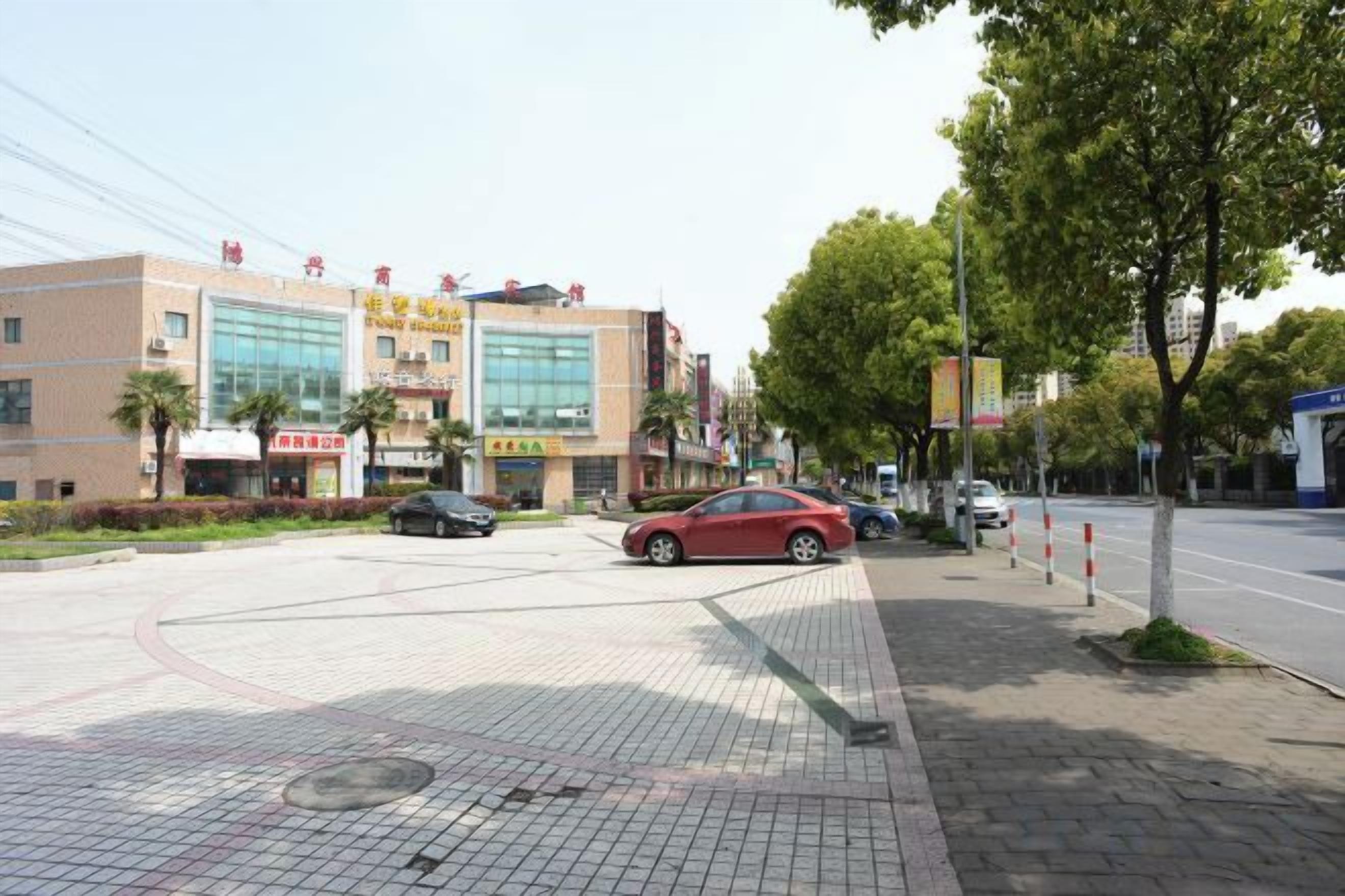 Een meerhoog gebouw met een glazen gevel, een parkeerplaats en een voetpad met bomen.