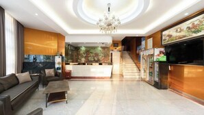 Un vestíbulo de hotel con una recepción, un sofá, una mesa de centro y una escalera que conduce a los pisos superiores.
